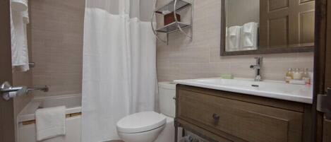 Un baño con ducha, inodoro, tocador y espejo.