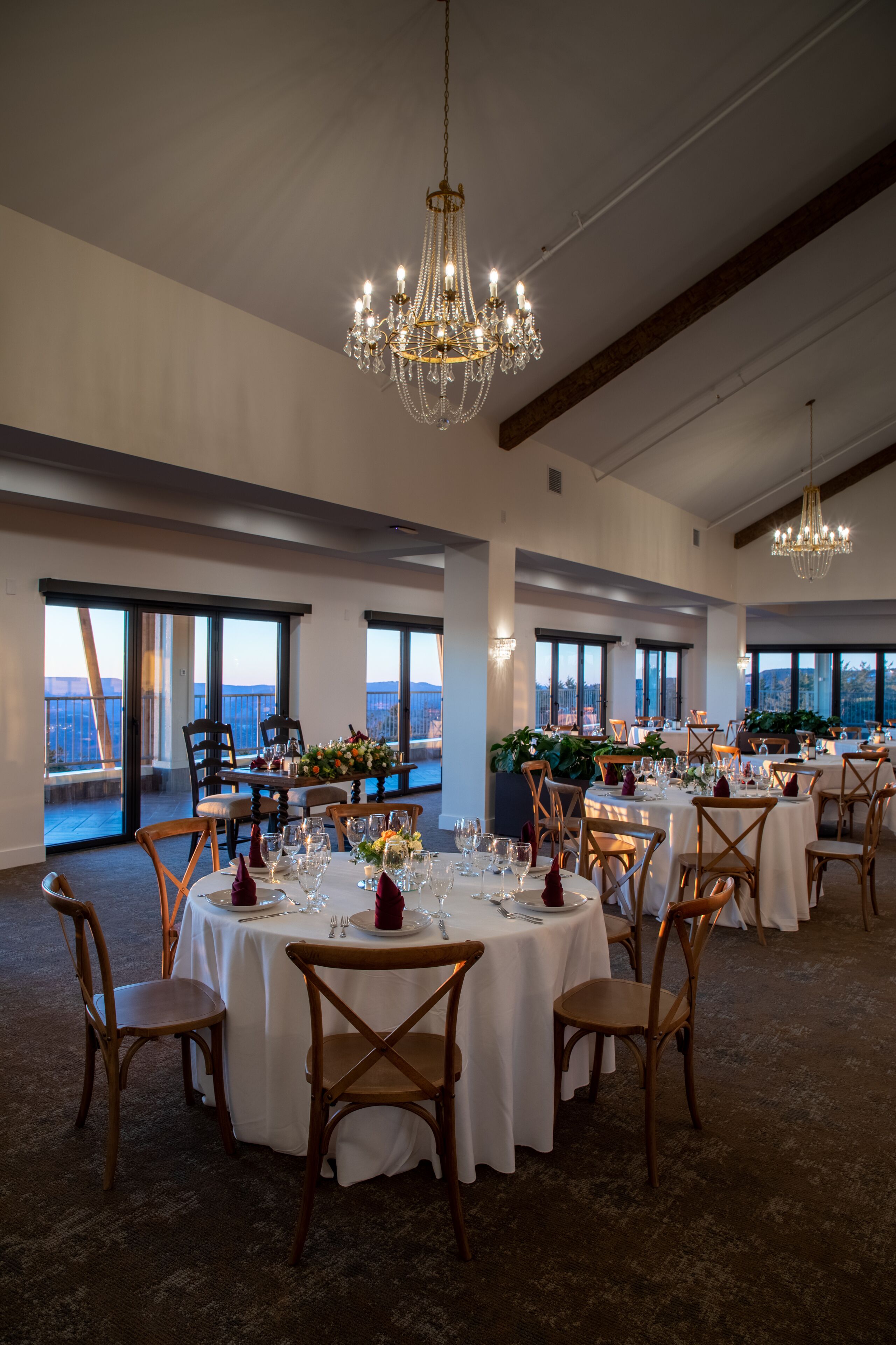 A spacious dining area with round tables, wooden chairs, and a chandelier. Large windows offer a view of the cityscape.