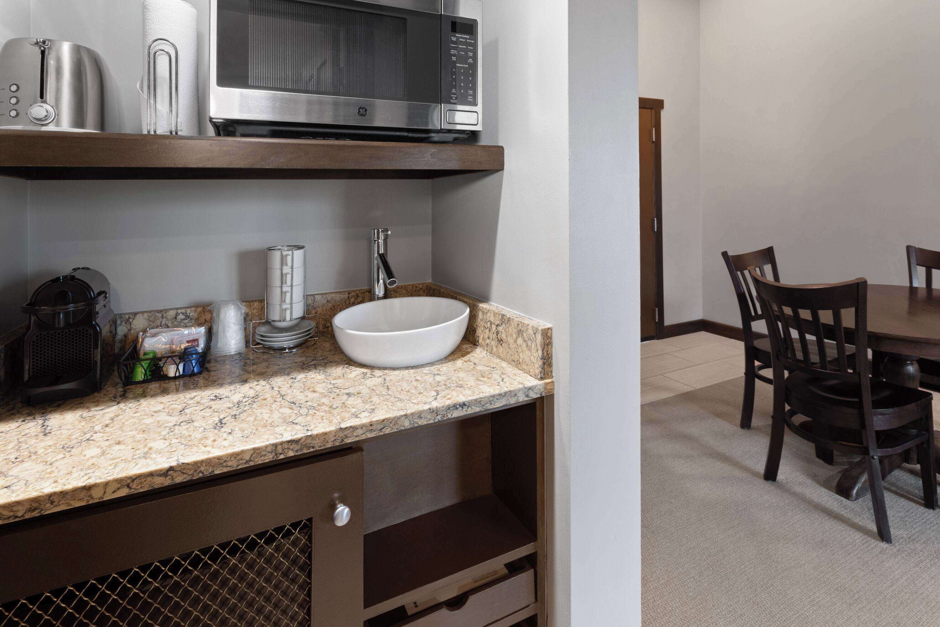 A kitchen with a granite countertop, a white sink, a stainless steel microwave, and a coffee maker.