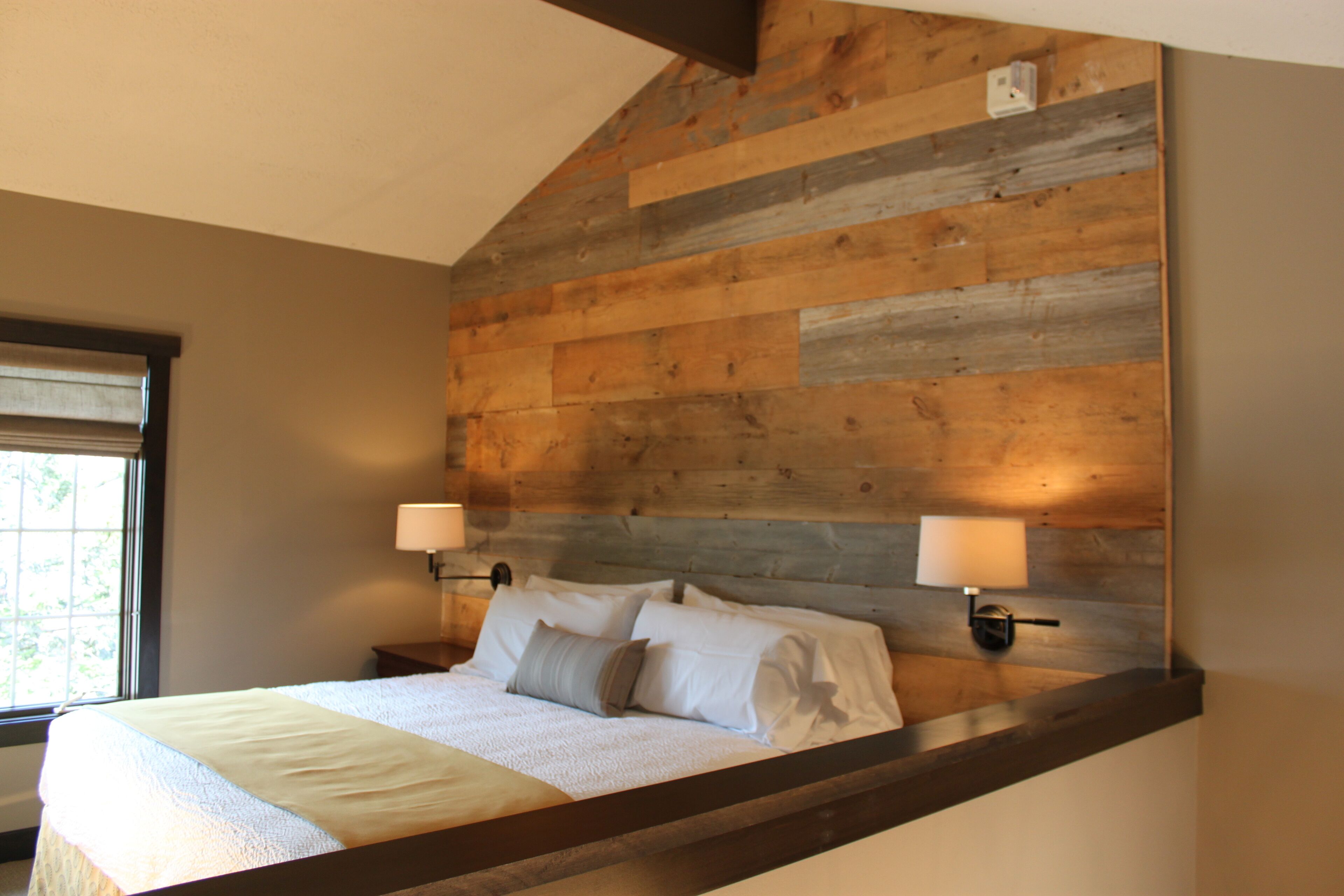 Un dormitorio con techo inclinado, cabecera de madera, dos lámparas de noche y una ventana.