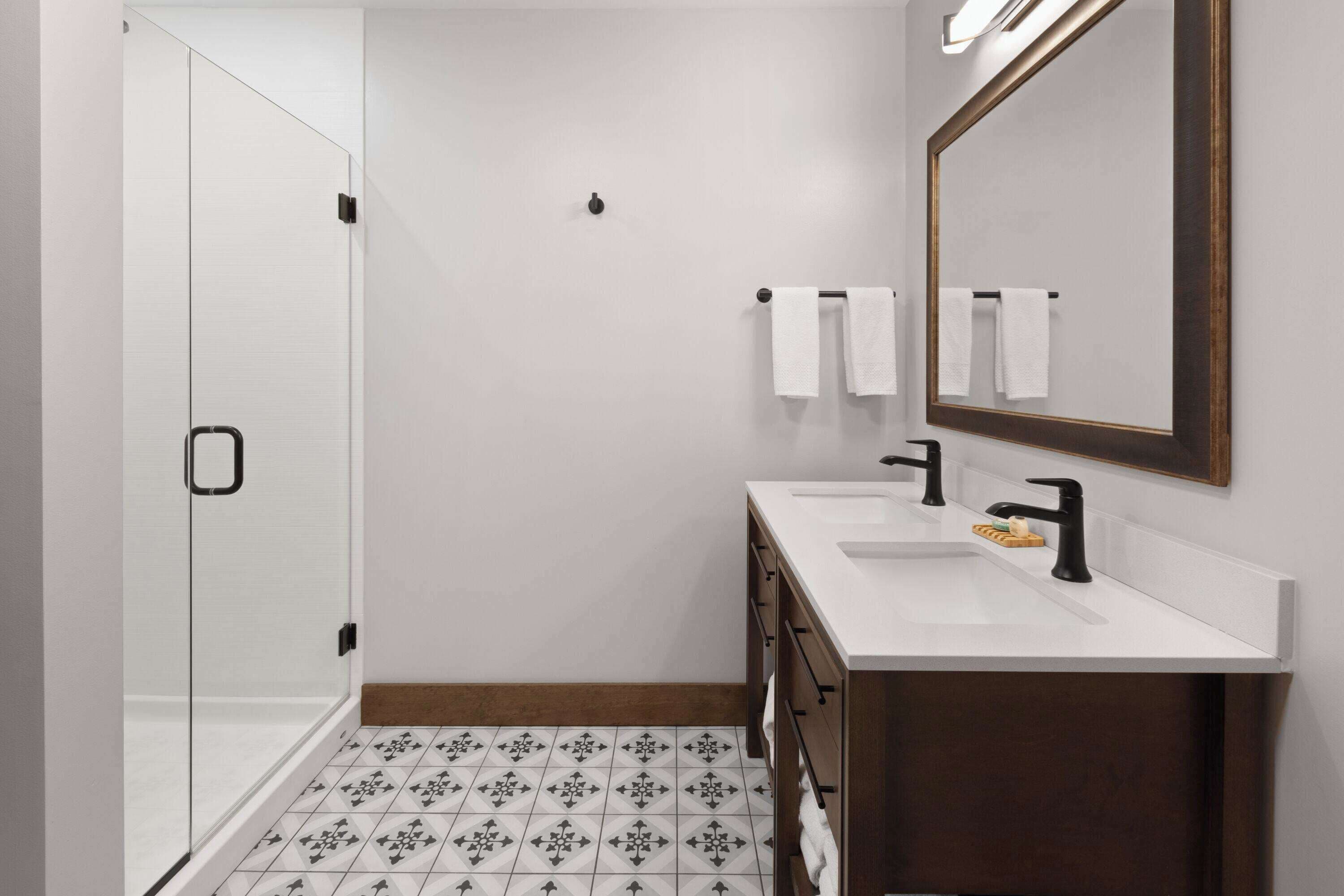 A modern bathroom with a glass shower, white tiles, a wooden vanity, and a large mirror.