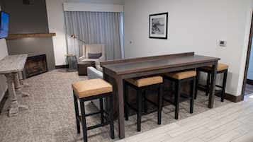 Una sala moderna con chimenea, una mesa de comedor con taburetes altos, un ventanal con cortinas y una obra de arte colgada.
