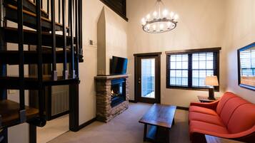 A living room with a stone fireplace, a red sofa, a wooden table, and a chandelier.