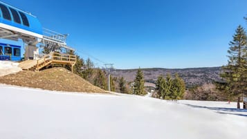 A ski lift with a blue cabin and wooden platform, surrounded by snow-covered slopes and trees.