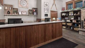 Een receptiegedeelte met een houten balie, een klok, planken met diverse spullen en een open haard met decoraties.