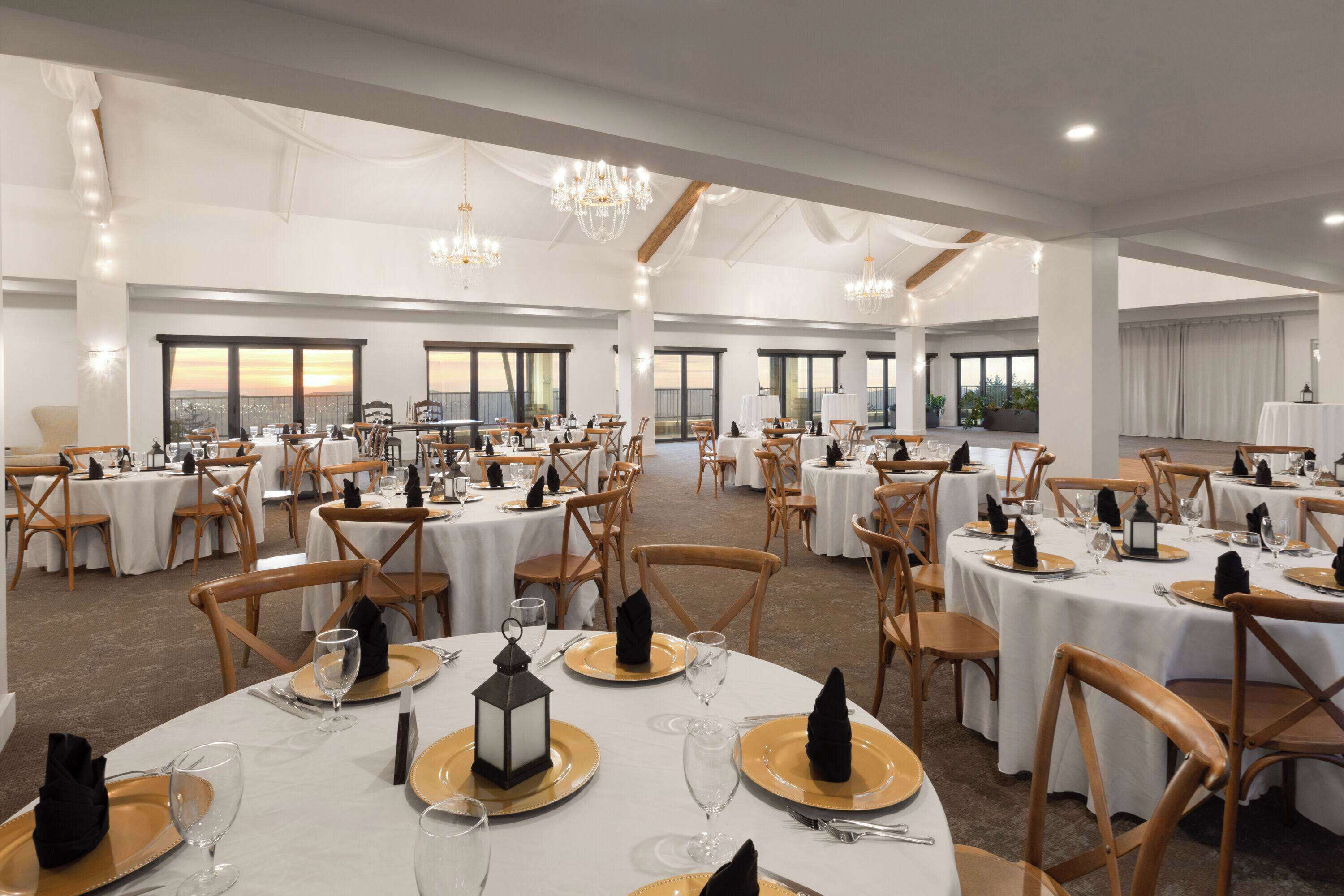 Un gran salón de banquetes con mesas redondas dispuestas para cenar, con manteles blancos y platos de carga dorados.