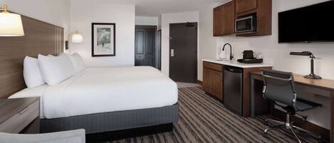 A hotel room with a large bed, a desk with a chair, a microwave, and a flat-screen TV.