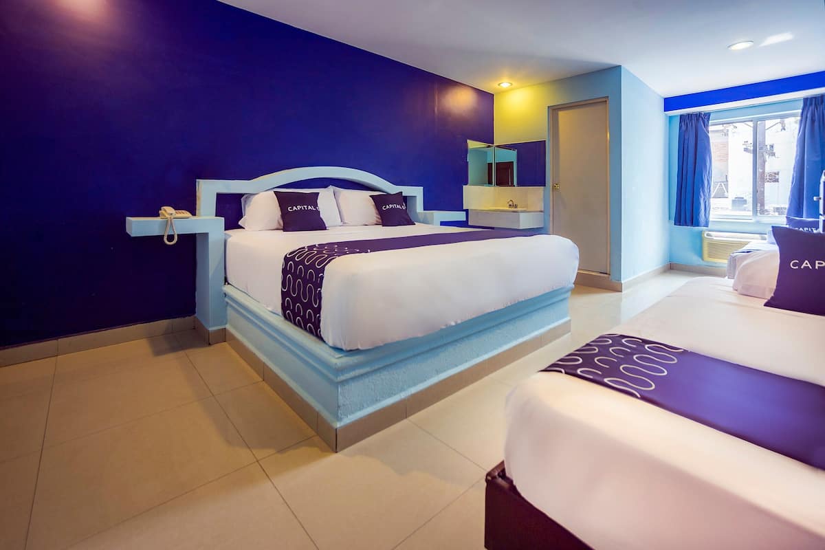 A modern hotel room with a large bed, a bedside table, a mirror, and a window with curtains.