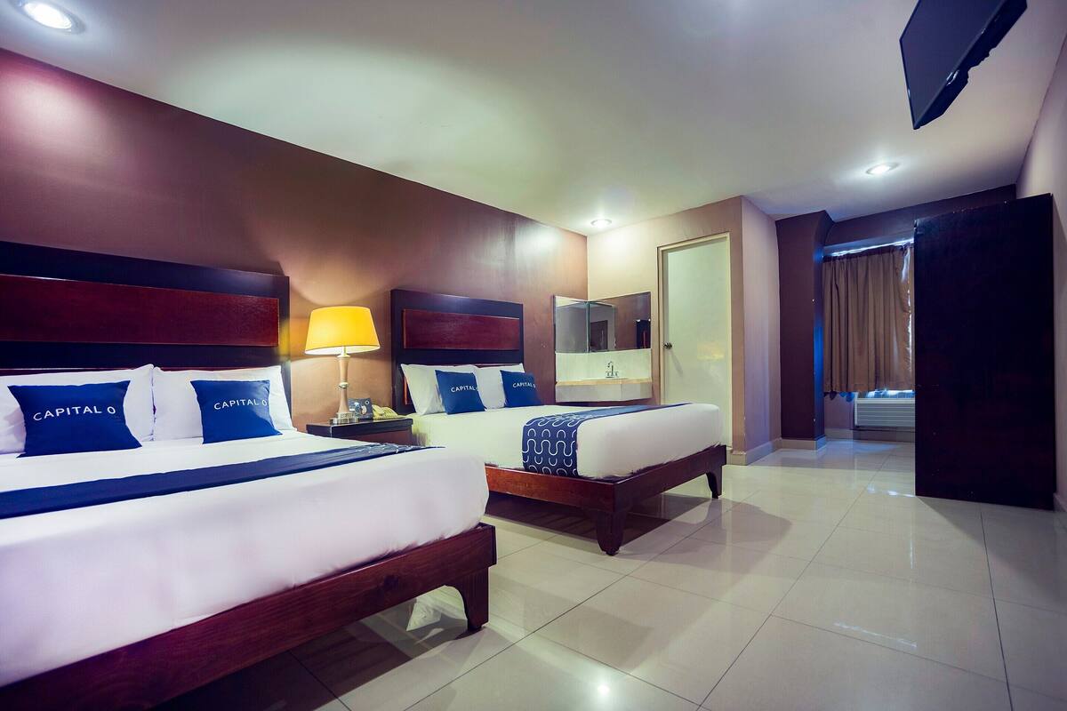 A hotel room with two beds, a nightstand, a lamp, a mirror, and a TV.