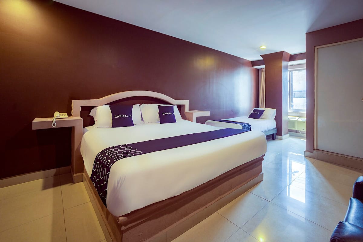A hotel room with a large bed, a smaller bed, a nightstand, and a view of the outside.