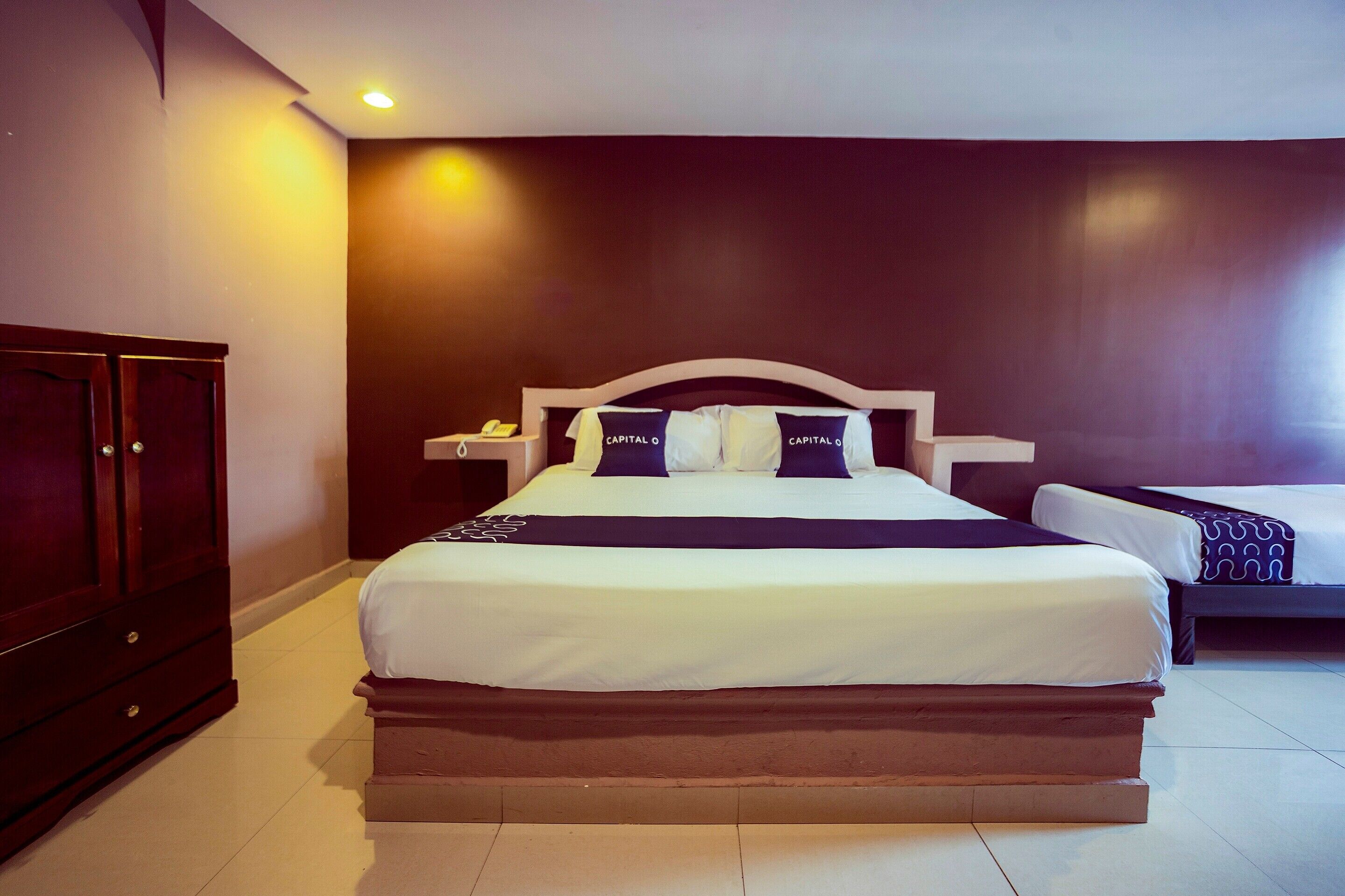 Habitación de hotel con una cama grande, una mesita de noche, un armario y una pared de color oscuro.