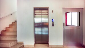 Un ascensor moderno con pantalla digital, una escalera y una puerta con ventanal.