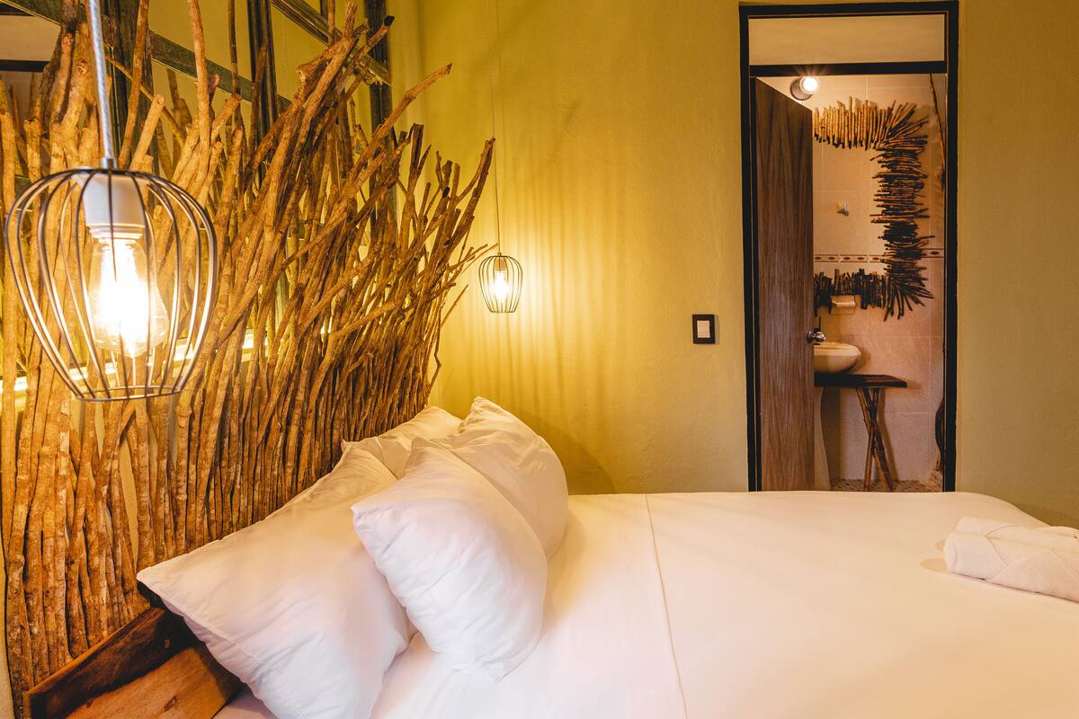 A bedroom with a bed, white pillows, a wooden headboard, and a wall-mounted light fixture.