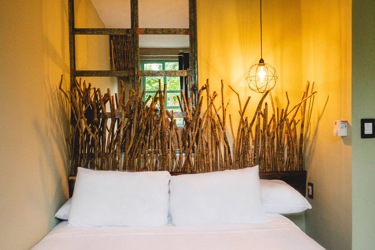 A bed with white linens and a plaid blanket, a wooden headboard, and a hanging light fixture.