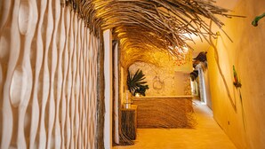 A narrow hallway with a rustic, woven ceiling and a stone wall. -  Straw Hat Tulum (Tulum)
