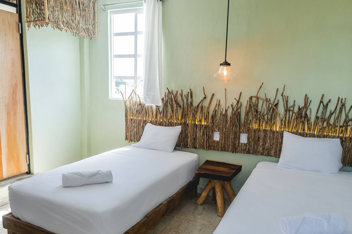 A room with two beds, a wooden headboard, a small wooden stool, and a hanging light fixture.