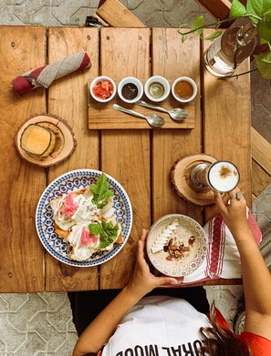 A wooden table with a plate of food, a glass of drink, and four small bowls of condiments. -  Straw Hat Tulum (Tulum)
