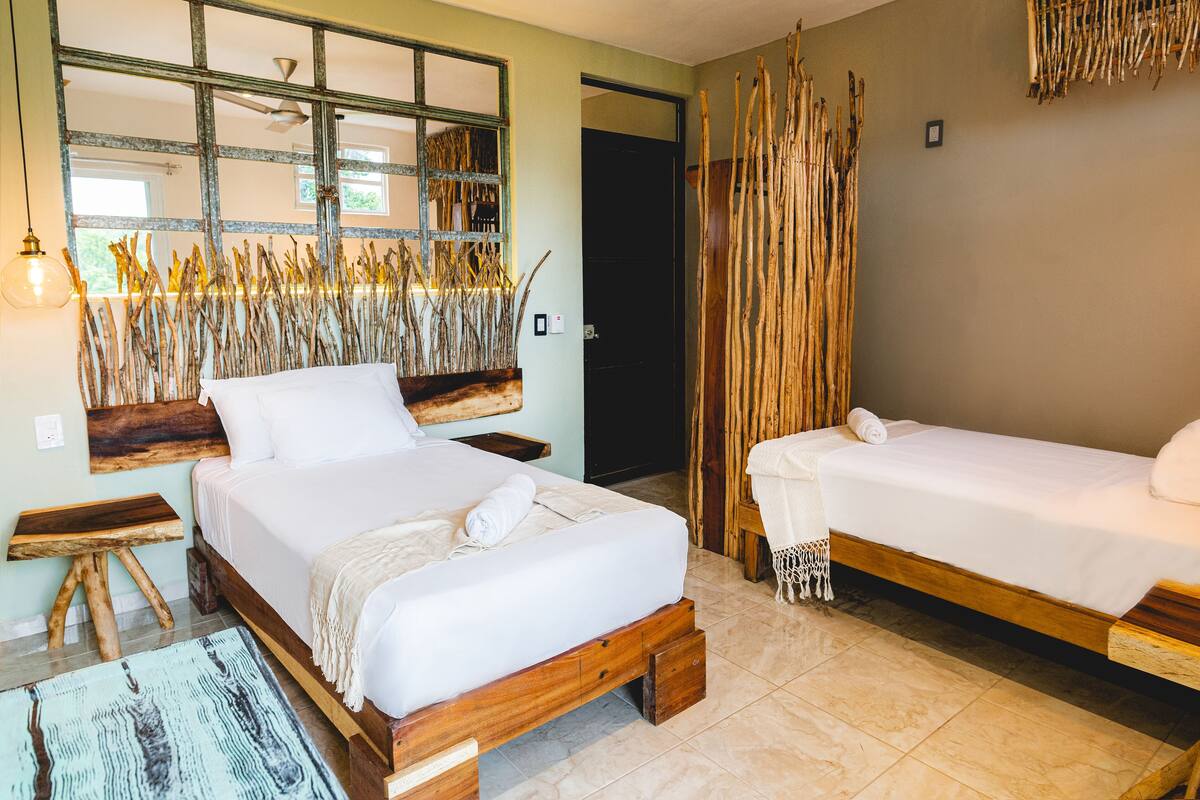 A room with two beds, a wooden headboard, a large window with a view, and a rustic decor theme.