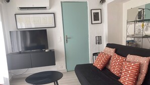 Ein Wohnzimmer mit einer schwarzen Couch, einem türkisfarbenen Sofa und einem Fernseher auf einem schwarzen Schrank.