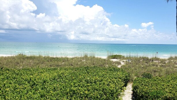 A beach with clear turquoise water, a sandy shore, and dense green vegetation in the foreground. - SunnyMar Retreat Beach Access • Heated Pool • Near Historic Bridge Street (Longboat Key)