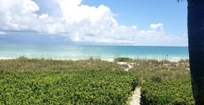 A beach with clear turquoise water, a sandy shore, and dense green vegetation in the foreground. - SunnyMar Retreat Beach Access • Heated Pool • Near Historic Bridge Street (Longboat Key)
