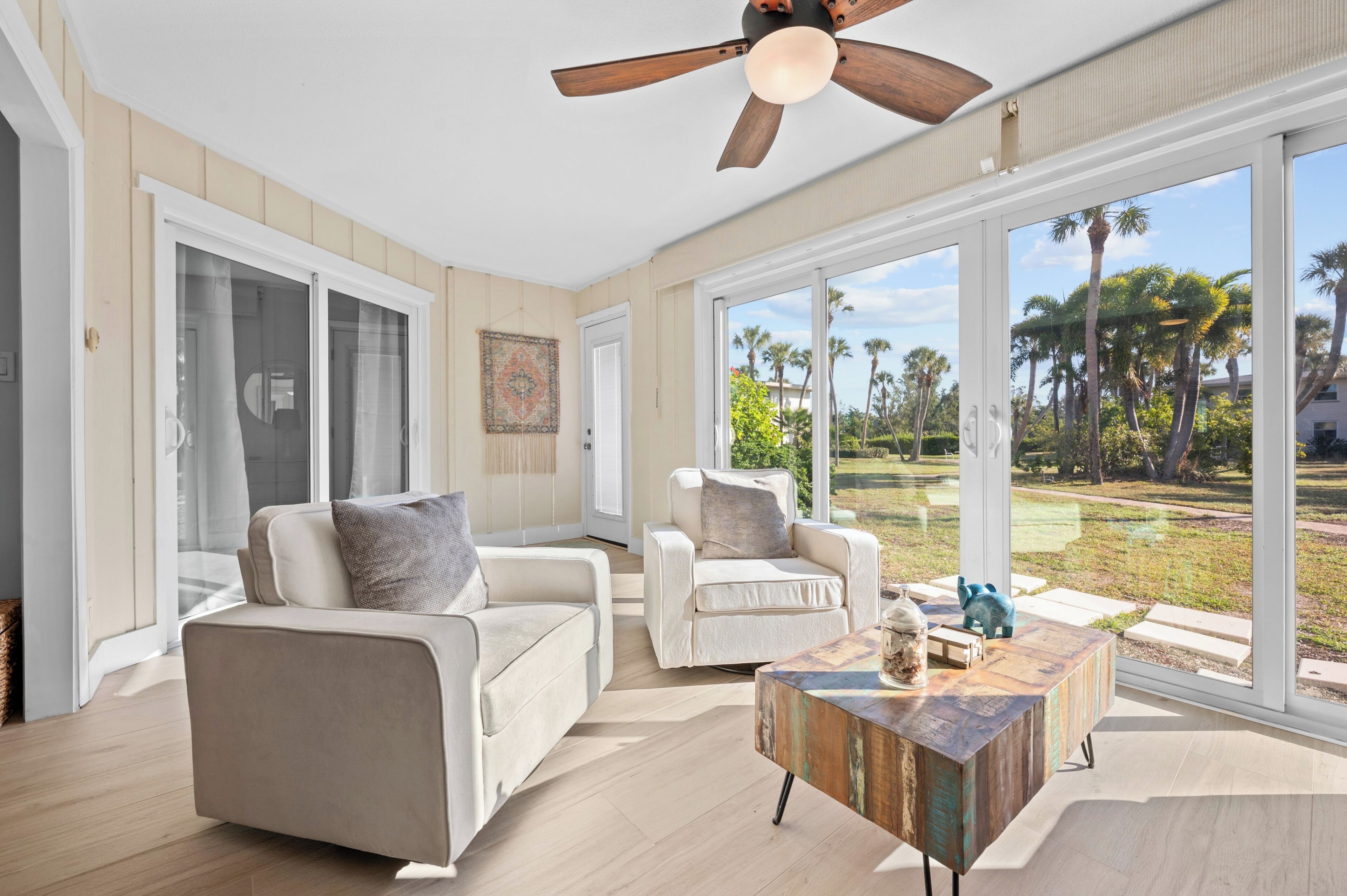 A spacious living room with a large window, a ceiling fan, and a wooden coffee table.