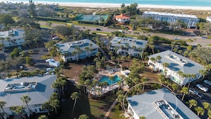 An aerial view of a coastal residential area with multiple houses, a swimming pool, and a beach in the background. - SunnyMar Retreat Beach Access • Heated Pool • Near Historic Bridge Street (Longboat Key)