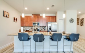 A modern kitchen with a central island, bar stools, stainless steel appliances, and pendant lighting.