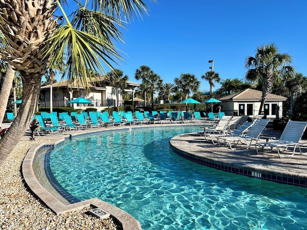 A pool with clear water, surrounded by lounge chairs and palm trees.