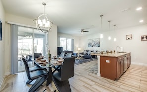 A modern kitchen with a central island, dining area with chairs and table, and a living room with a sofa and coffee table.