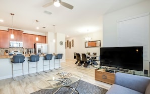 A modern kitchen with stainless steel appliances, a dining area with a glass table, and a living room with a flat-screen TV.