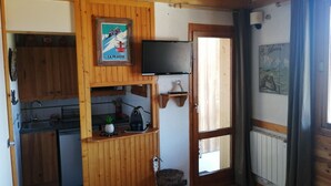 A wooden interior with a kitchen area, a mounted TV, and a door leading outside.