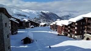A snow-covered mountain resort with multi-story buildings, ski slopes, and a clear sky.
