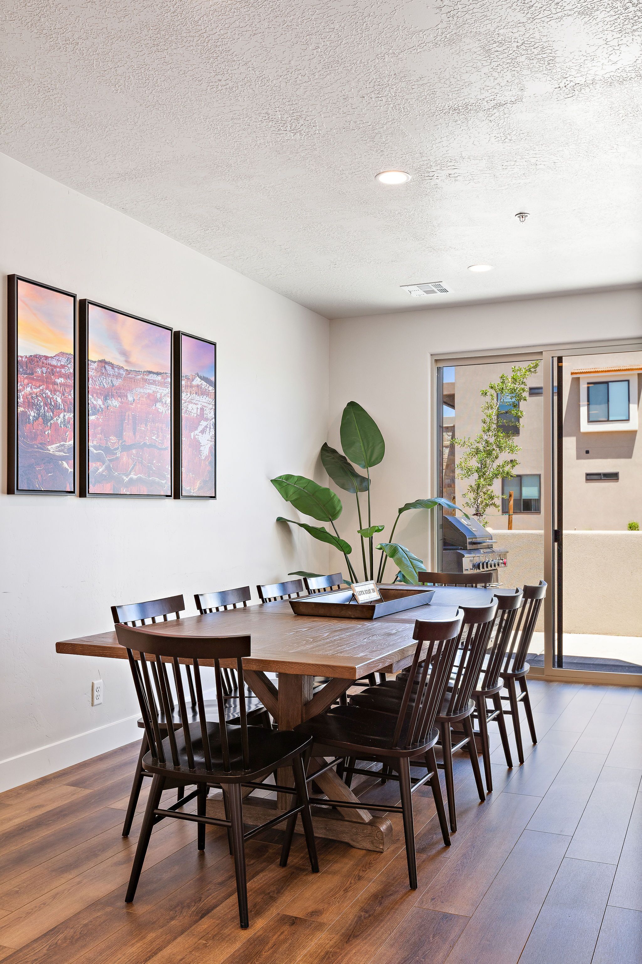 Un coin repas avec une table et des chaises en bois, une grande plante et trois tableaux encadrés accrochés au mur.
