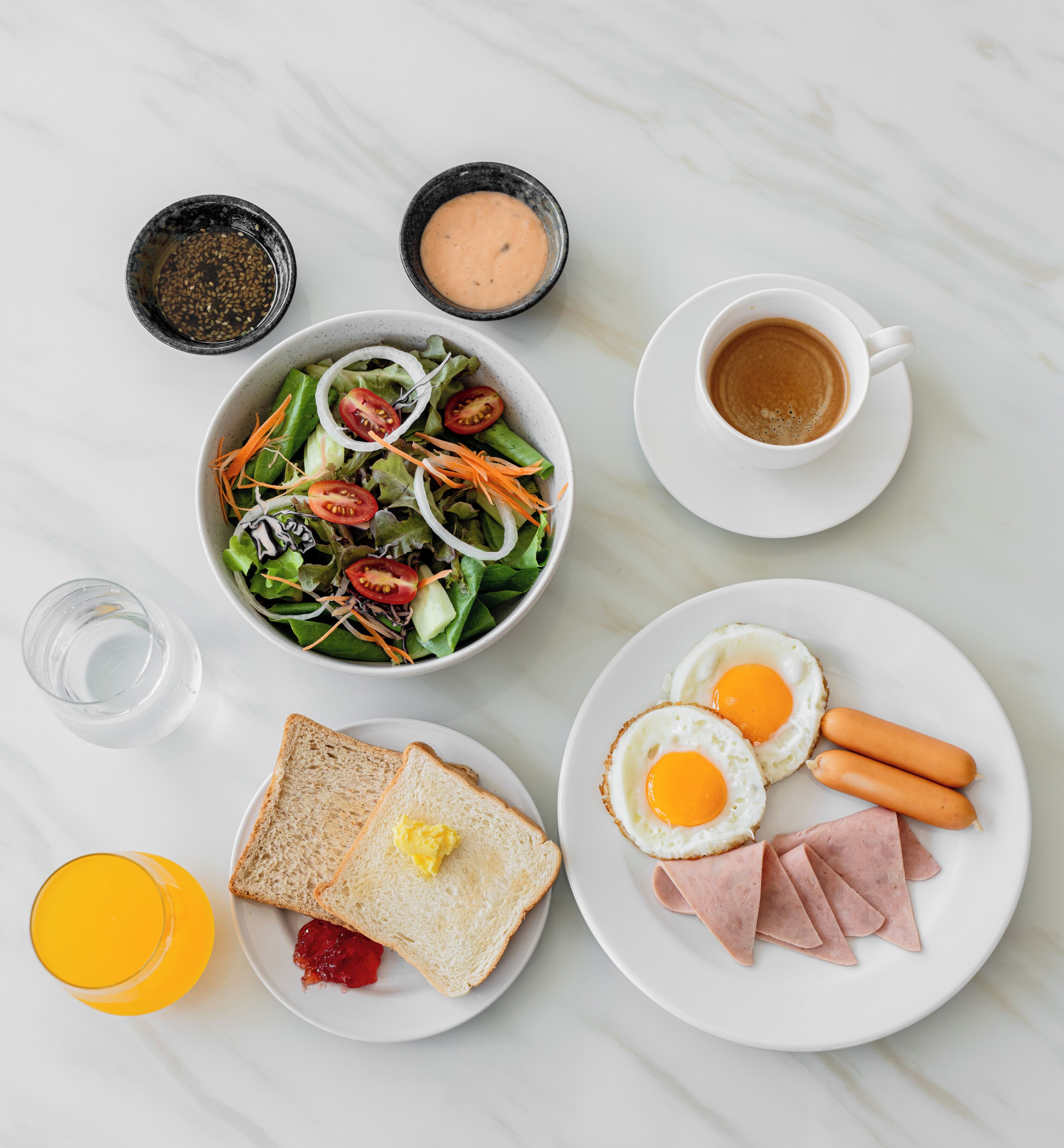 Un desayuno con ensalada, huevos, jamón, tostadas y café.
