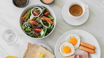 Un desayuno con ensalada, huevos, jamón, tostadas y café.