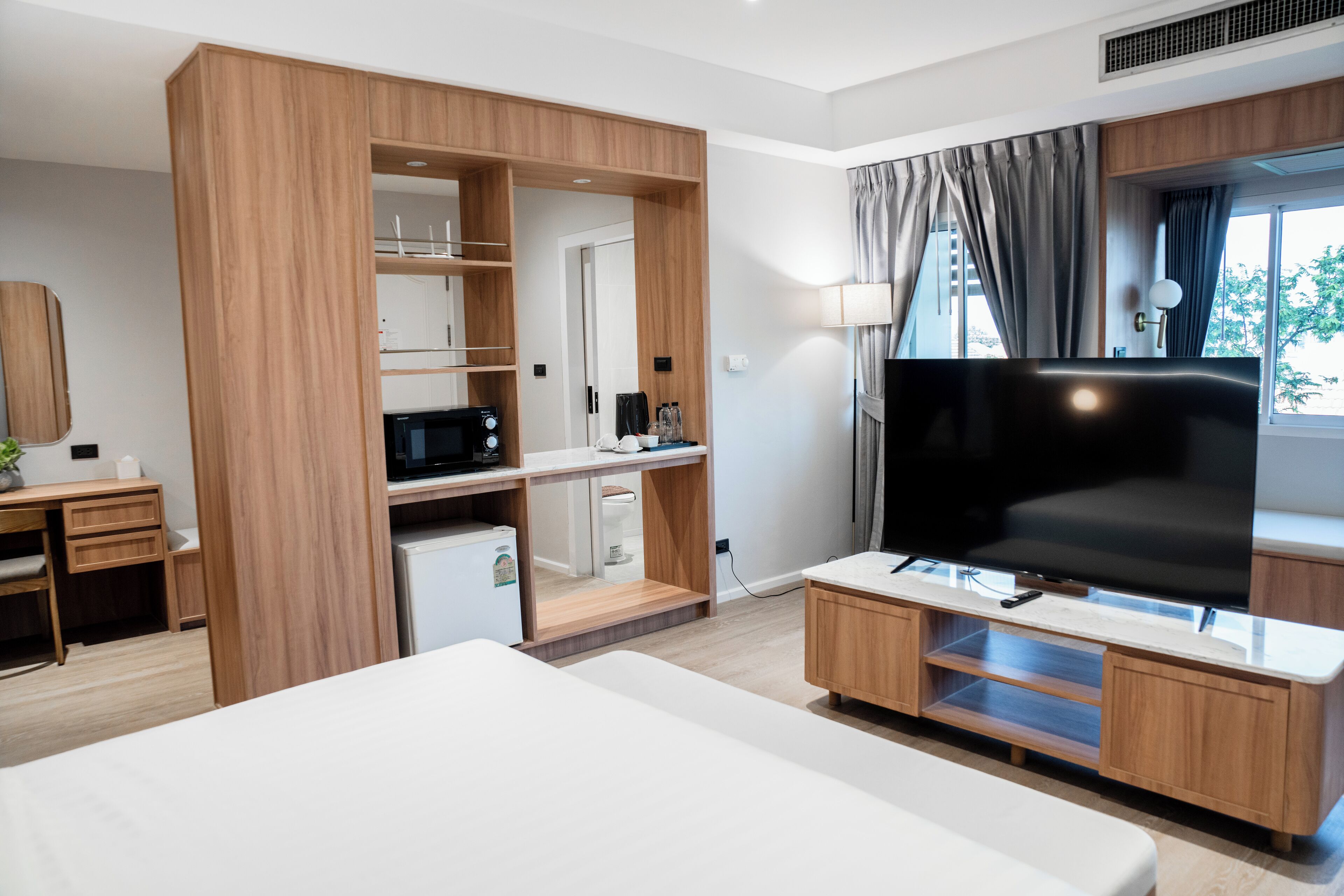 Una habitación de hotel moderna con una cama grande, televisión, escritorio con computadora, armario y una pequeña kitchenette.