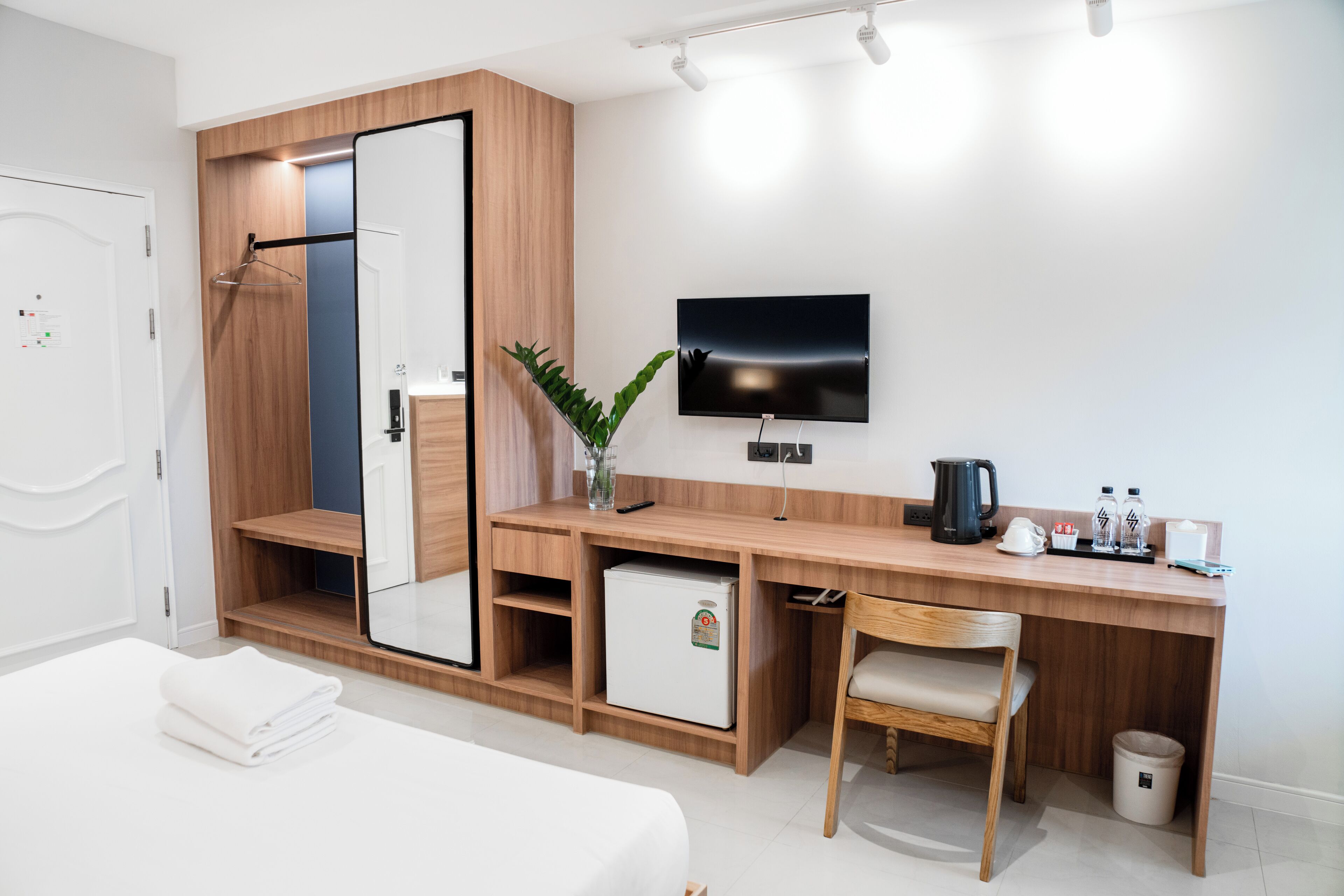 A modern hotel room with a bed, a wooden desk, a television, and a small refrigerator.