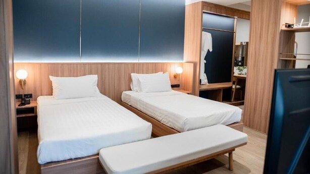 Habitación de hotel con dos camas individuales, un banco, un armario y un espejo.