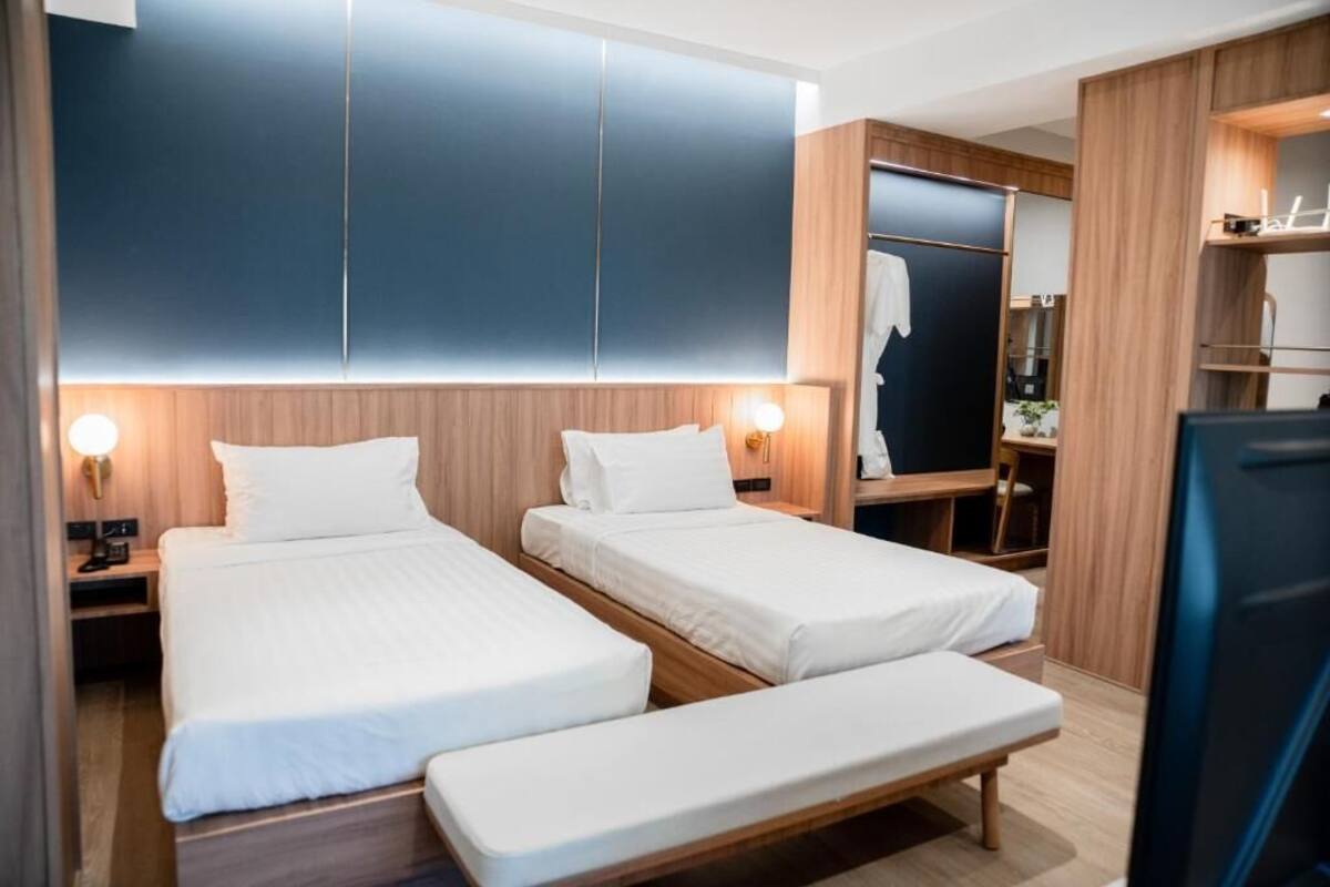 Een hotelkamer met twee eenpersoonsbedden, een bankje, een kledingkast en een spiegel.