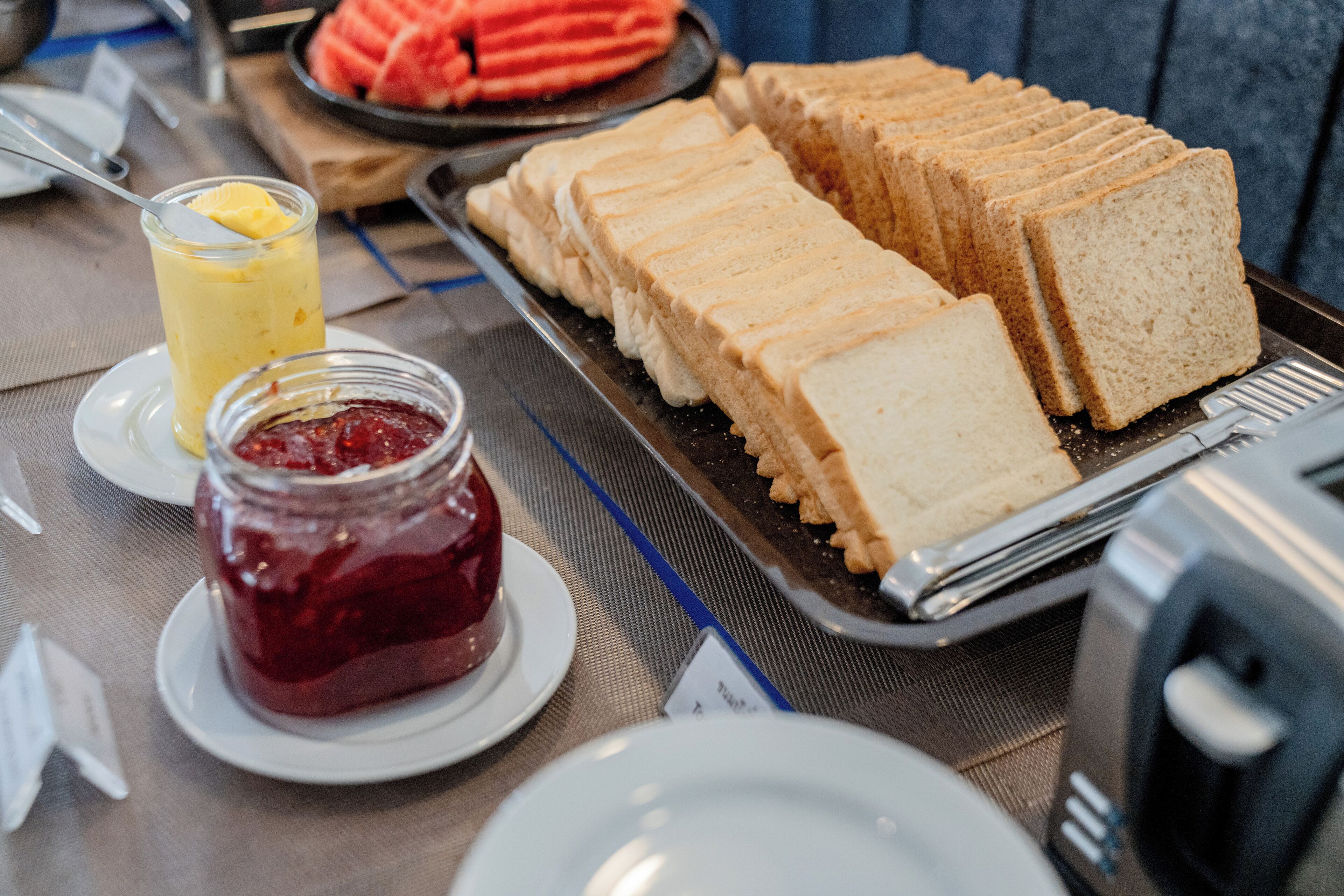 Un bufé de desayuno con pan en rodajas, un vaso de jugo y un frasco de mermelada.