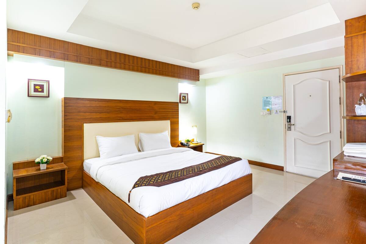Een hotelkamer met een houten bed, een nachtkastje, een bureau en een deur.