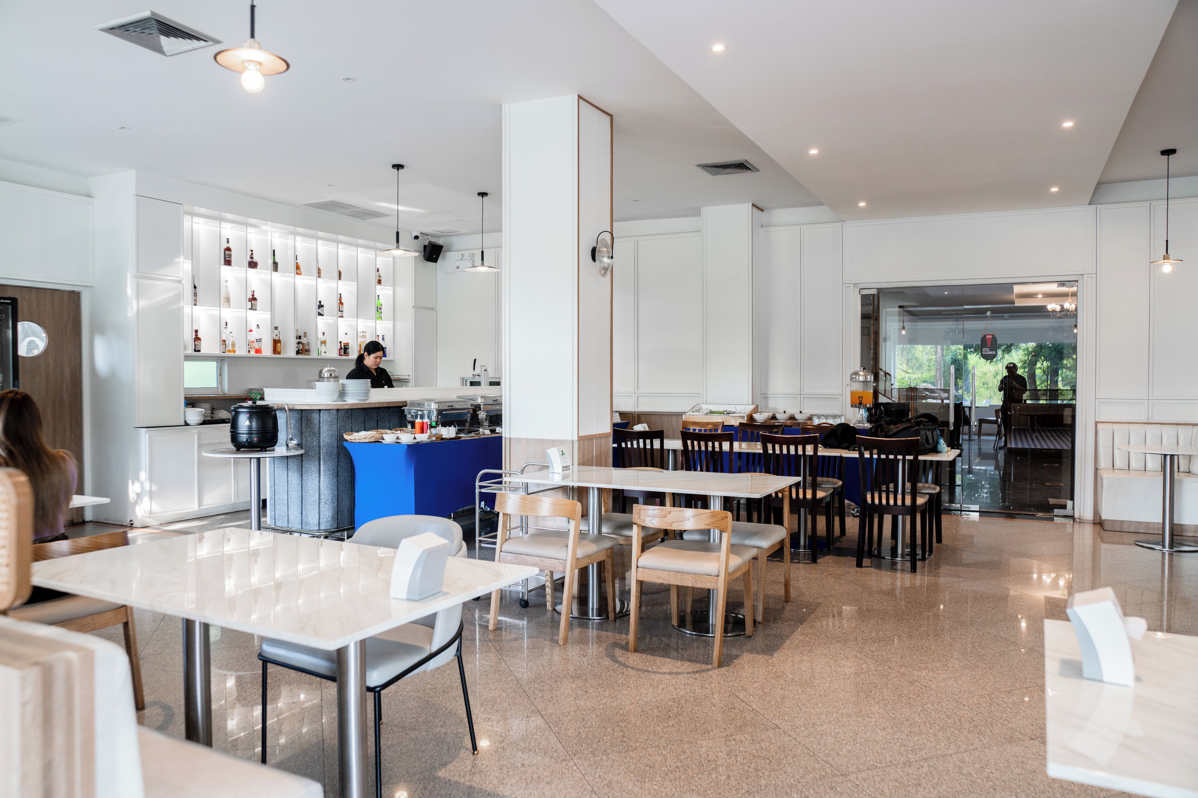 A modern restaurant with a bar area, seating arrangements, and a kitchen visible in the background.