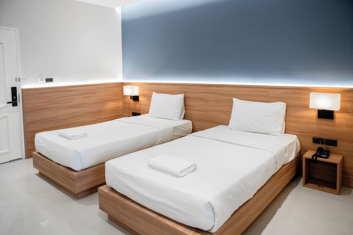 Hotelkamer met twee enkele bedden, houten hoofdborden, nachtlampjes en een klein nachtkastje met een telefoon.