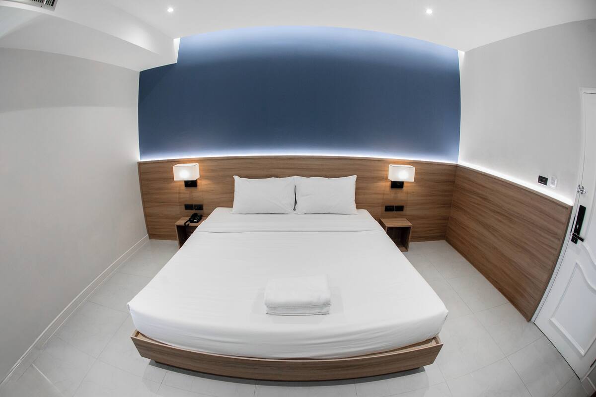 Een moderne hotelkamer met een groot bed, een houten hoofdeinde en twee bedlampjes.