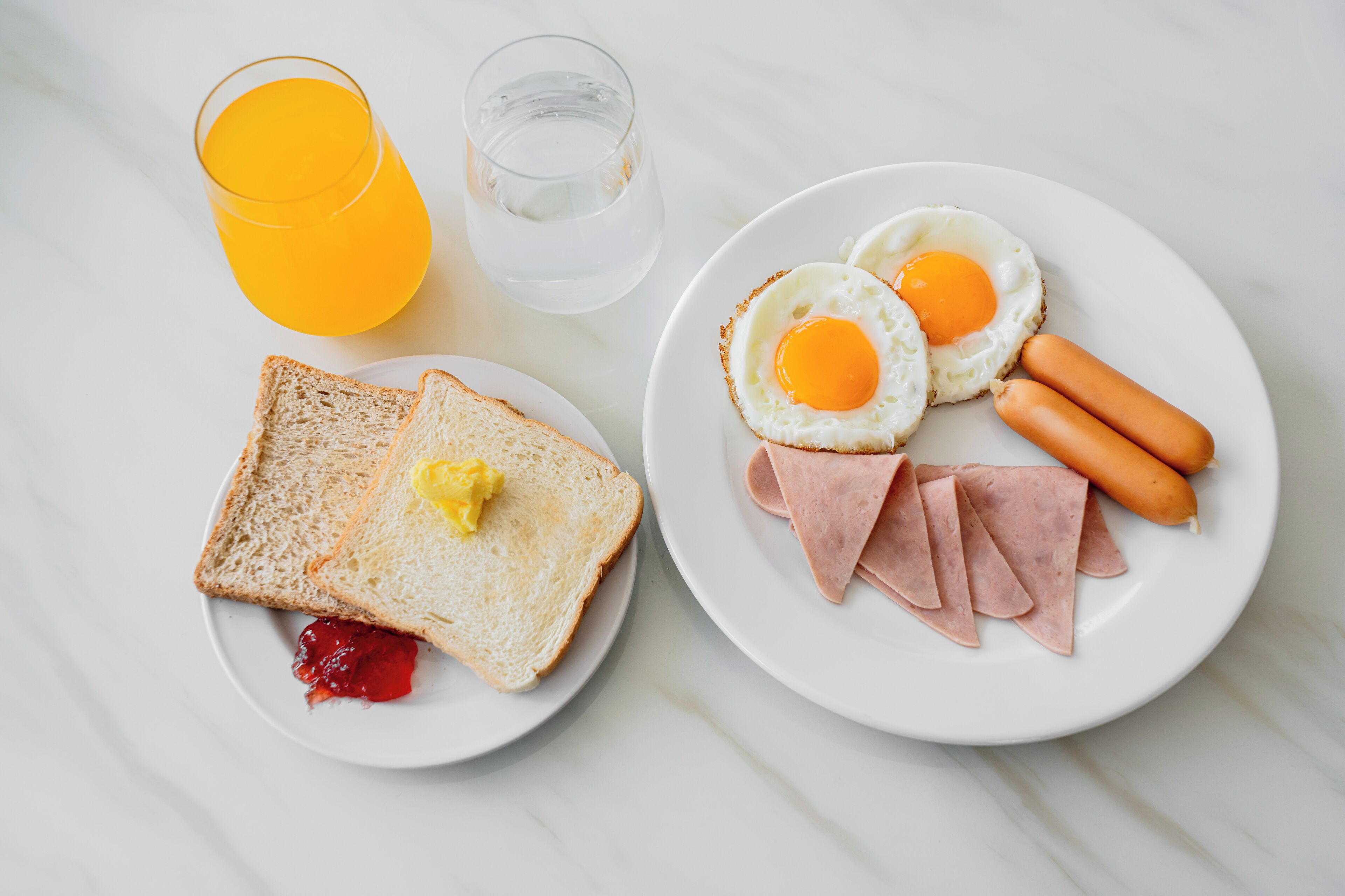 A breakfast plate with toast, jam, two fried eggs, ham, and sausages.
