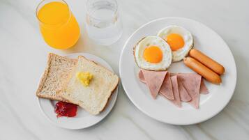 A breakfast plate with toast, jam, two fried eggs, ham, and sausages.