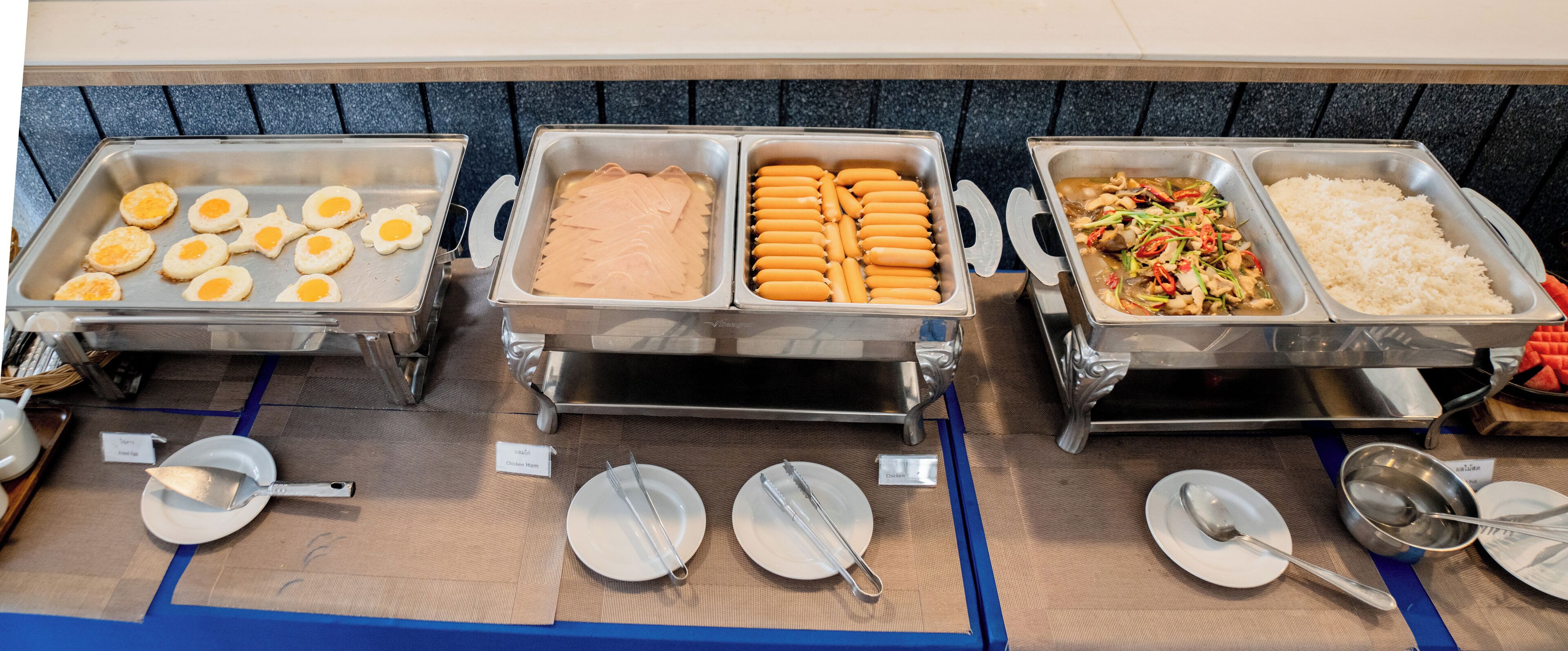 A buffet with labeled sections for eggs, chicken ham, hot dogs, and a stir-fry dish.