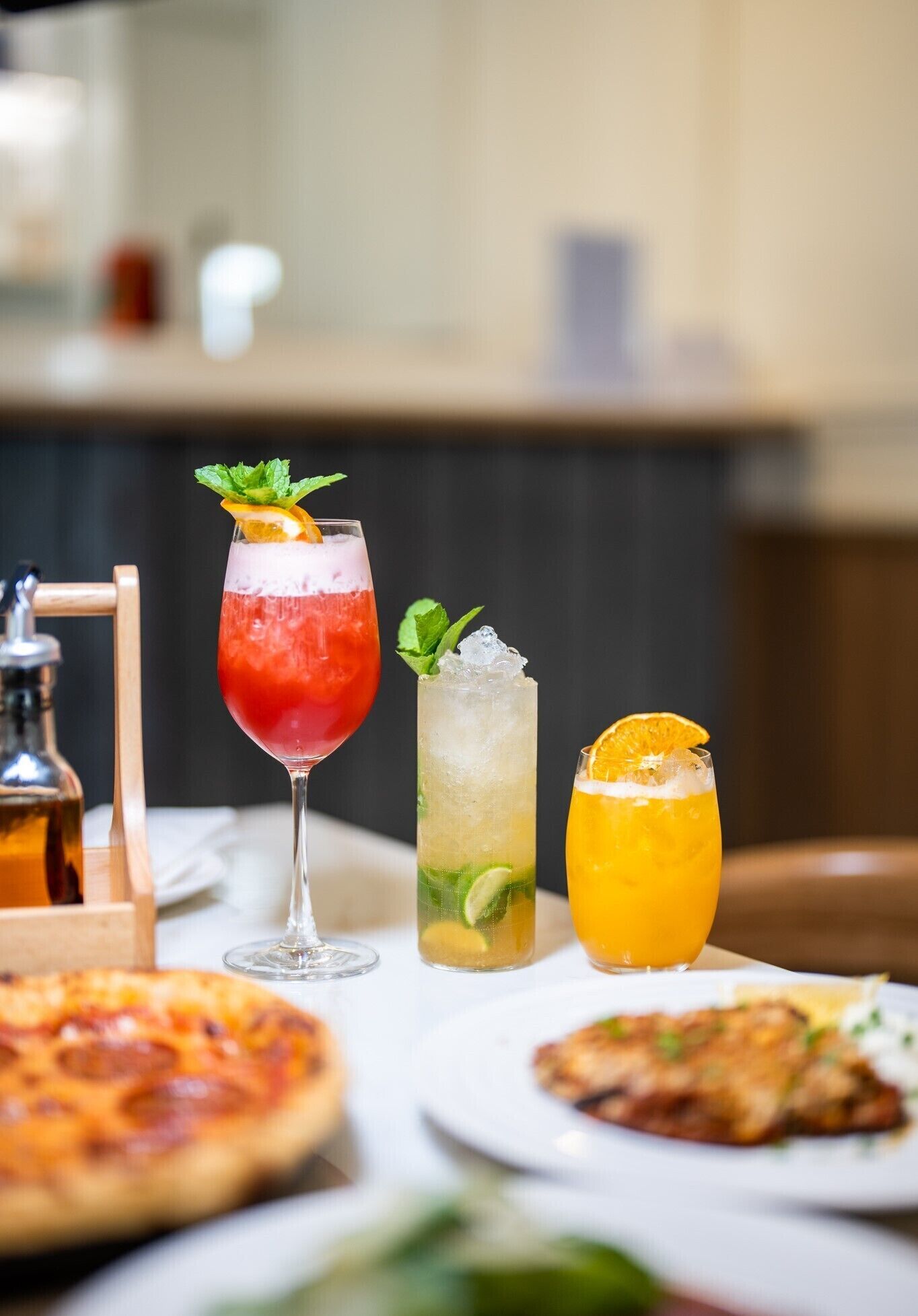 A table with three drinks, a pizza, and a dish with meat.