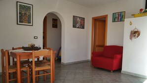 En matplats med ett träbord och stolar, en röd soffa och en hall med en dörr som leder till ett annat rum.